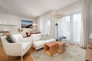 Ein modernes Wohnzimmer mit einer Couch, zwei Holztischen, einem Couchtisch und einem Essbereich im Hintergrund.