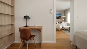 Una camera moderna con una scrivania in legno, una sedia marrone, una lampada e un letto con copripiumino fantasia.