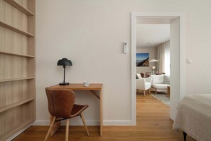 Ein modernes Zimmer mit einem Holztisch, einem braunen Sessel, einer Lampe und einem Bett mit gemustertem Überwurf.