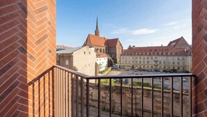 Vista da un balcone su un edificio storico con una torre imponente, una strada lastricata e auto parcheggiate.