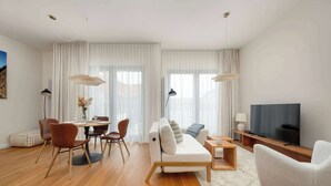 Un soggiorno moderno con divano, tavolo da pranzo, sedie, televisore e ampie finestre con tende leggere.