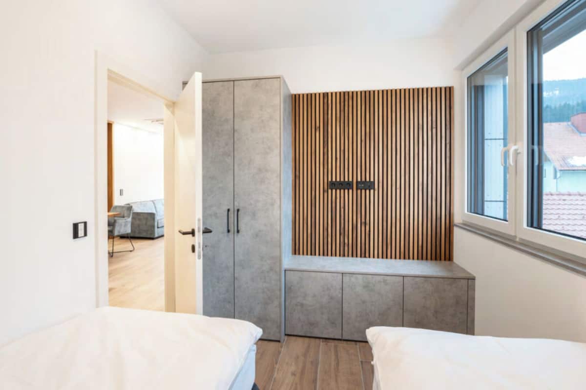 A modern bedroom with two beds, a wardrobe, and a window with a view.
