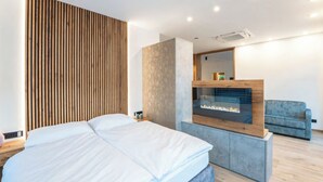 A modern hotel room with a bed, a seating area with a fireplace, and a large mirror. - Lorenzer Penthouse (Scheifling)