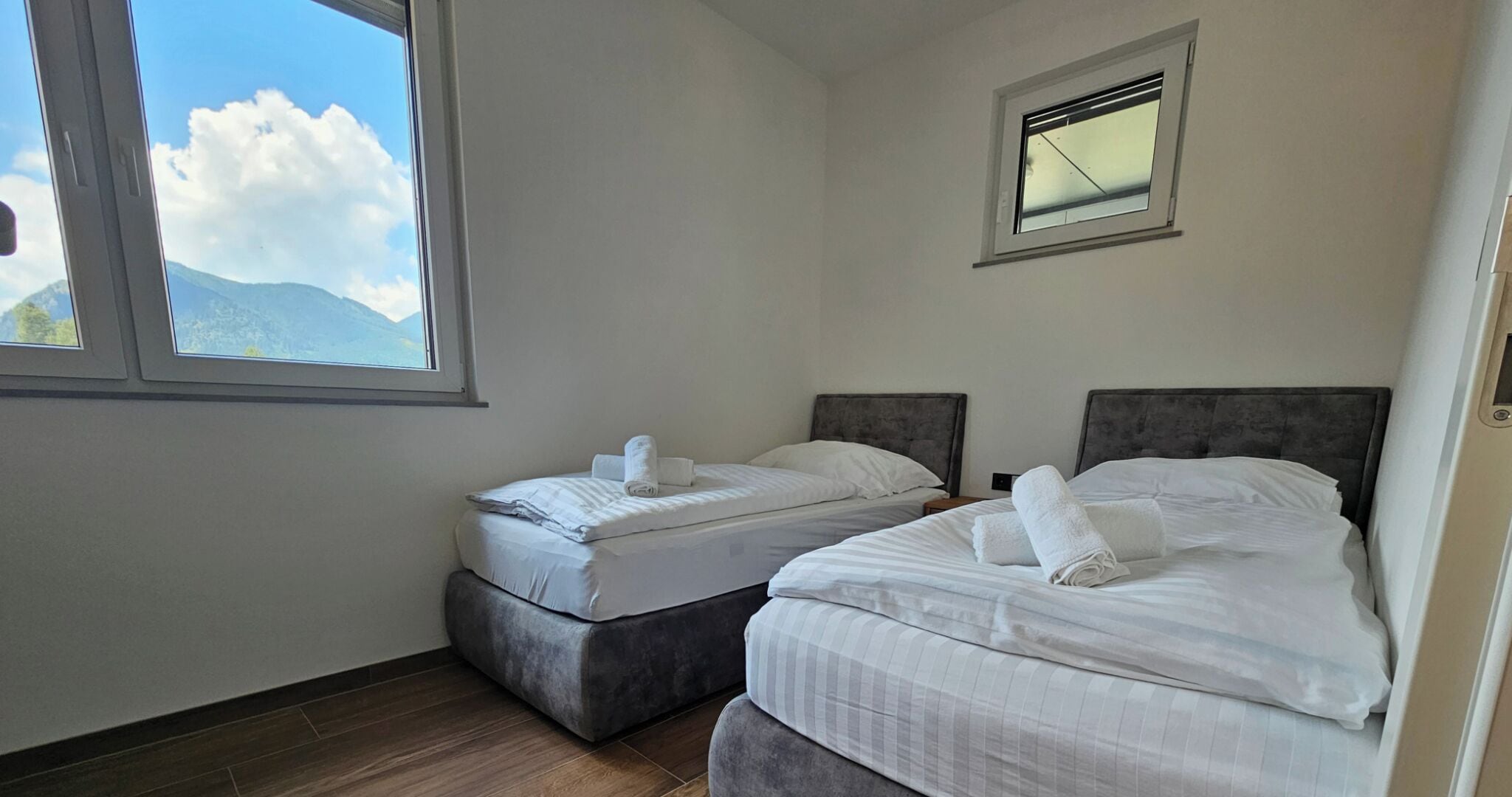 A hotel room with two beds, a window with a mountain view, and a small window above the beds.