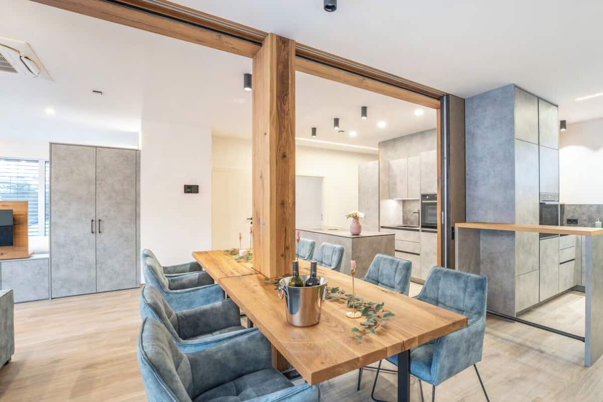 A modern dining area with a wooden table, blue chairs, and a kitchen in the background.