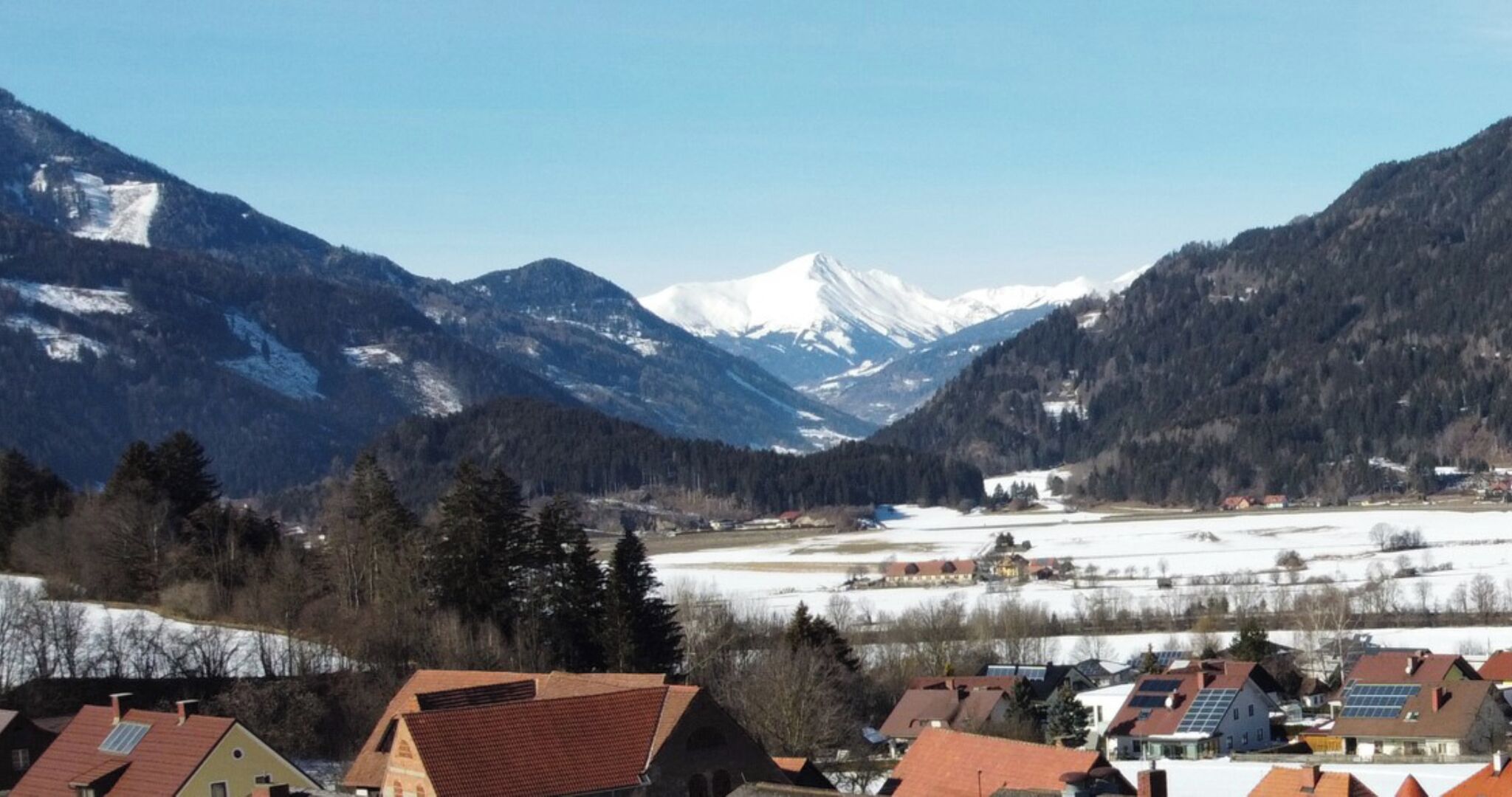 Un paisaje montañoso con picos nevados, un valle con edificios y un río.