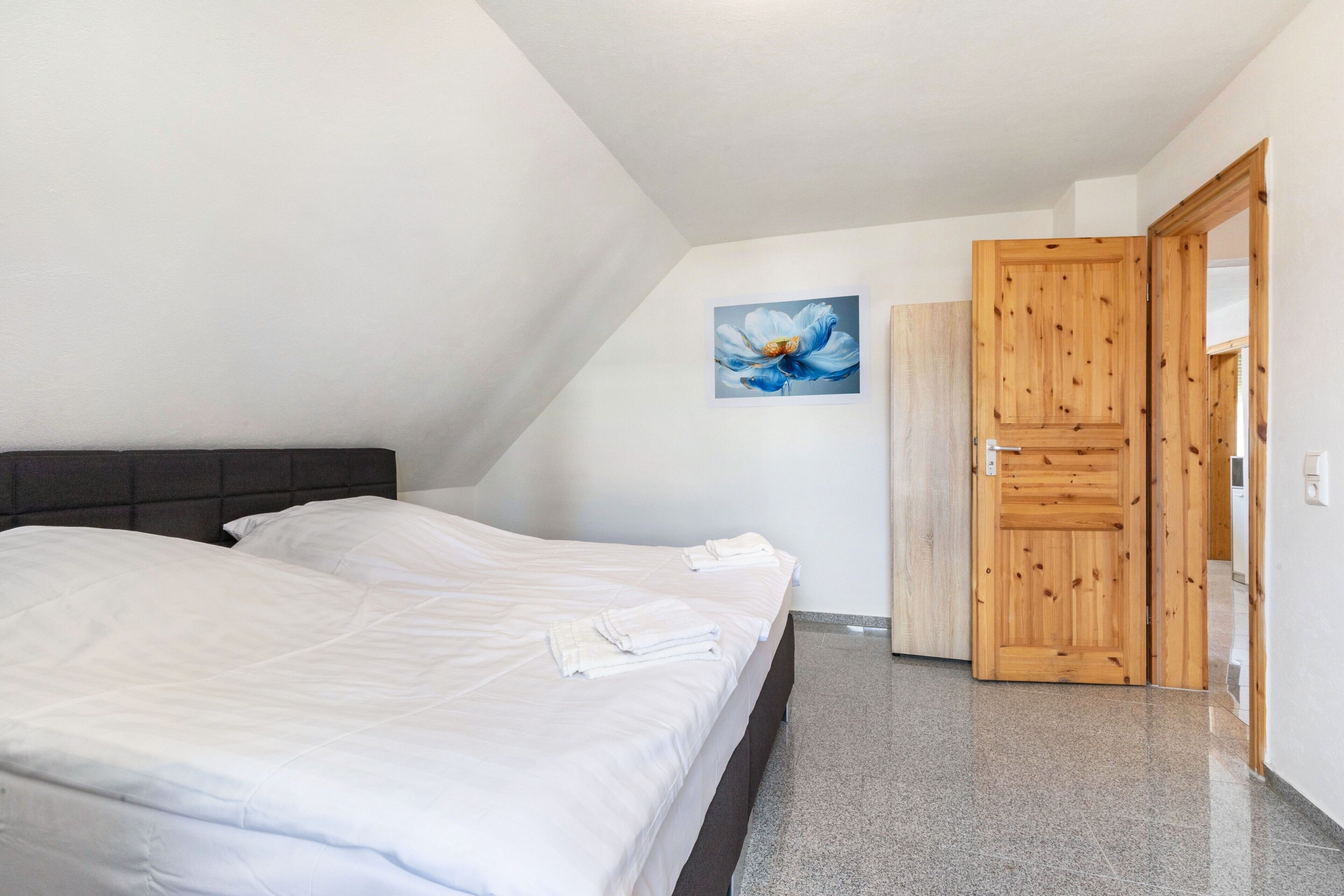 Une chambre à coucher avec un lit, une armoire en bois, un tableau et une porte.