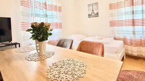 A hotel room with a bed, a TV, a dining table with placemats, and curtains with a striped pattern. - Apartment 'Gemütliche' with Wi-Fi (Göppingen)