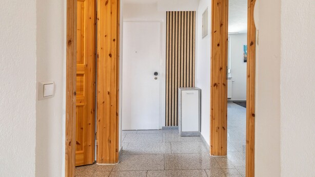 A hallway with wooden doors, a white wall with a vertical wooden panel, and a small white appliance. - Apartment 'Gemütliche' with Wi-Fi (Göppingen)