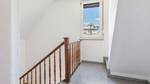 A stairwell with a wooden railing, a small window with a view of buildings, and a white wall. - Apartment 'Gemütliche' with Wi-Fi (Göppingen)
