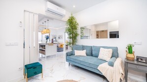 A modern living room with a sofa, a small table, a plant, and a kitchen in the background. - Mar & Sol Penthouse Portimão with Sea View, Wi-Fi, and Air Conditioning (Portimão)
