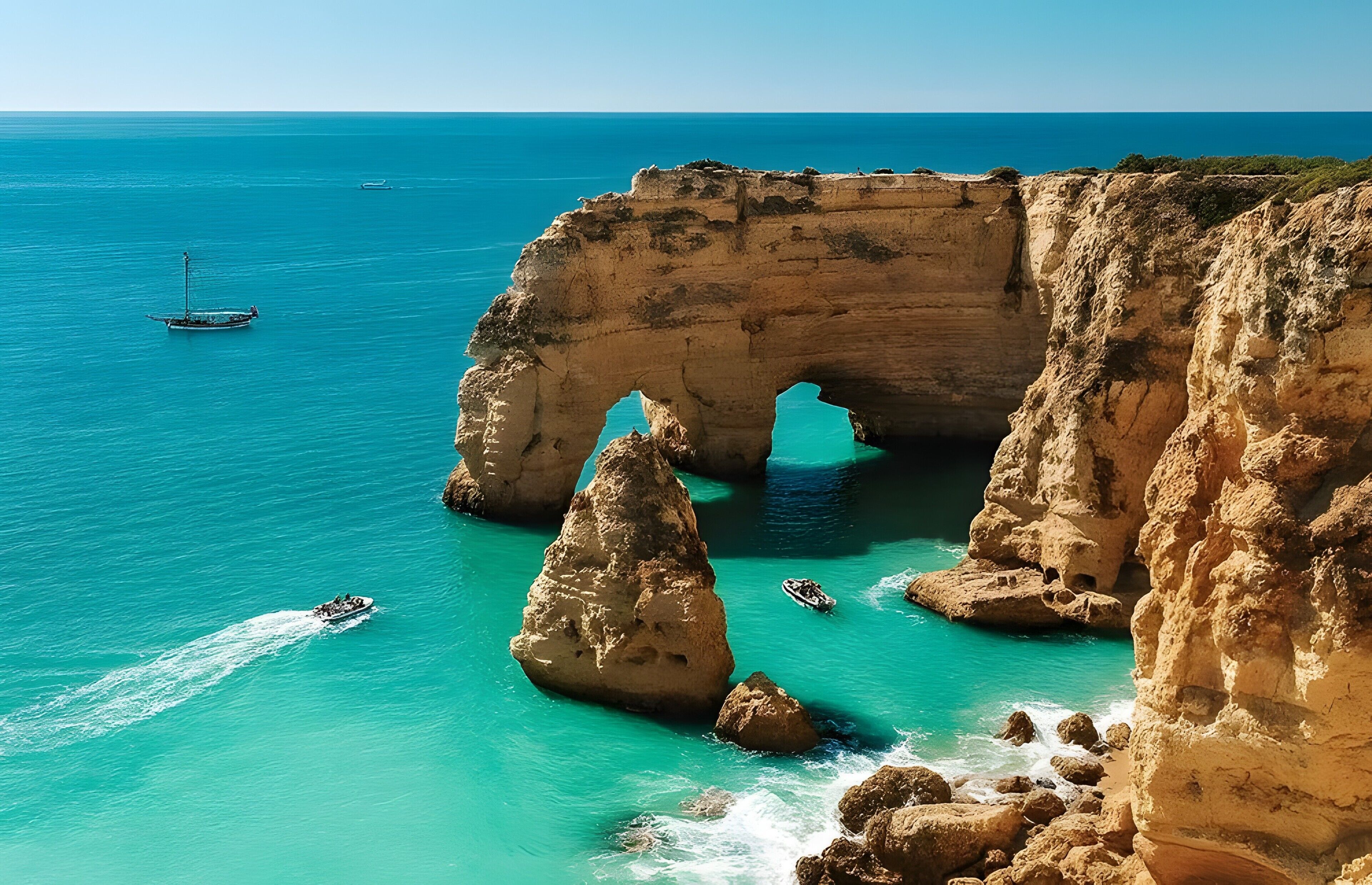 A coastal landscape with a natural rock arch formation, clear turquoise waters, and boats.