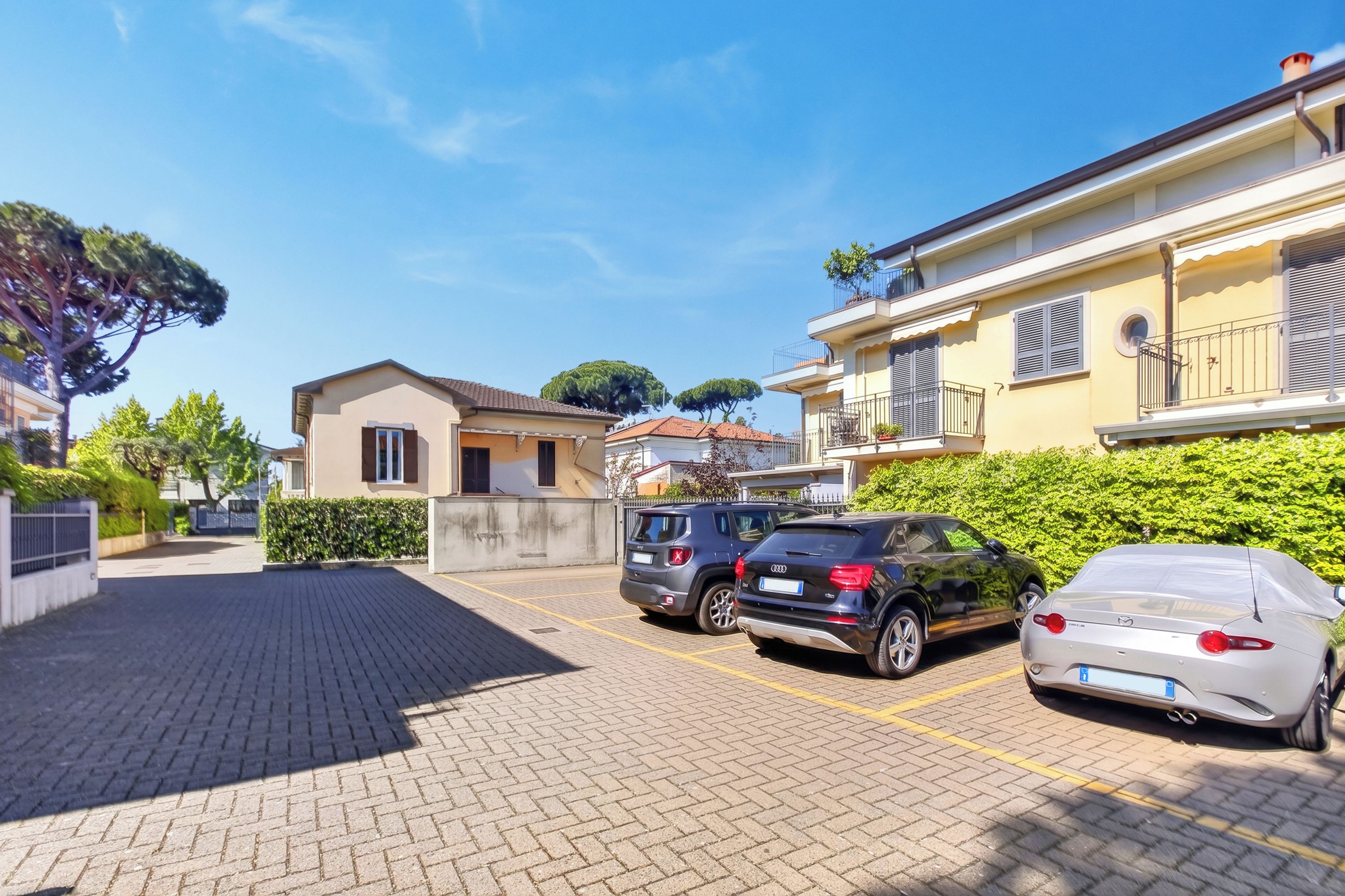 A residential area with parked cars, a paved driveway, and a building with balconies.