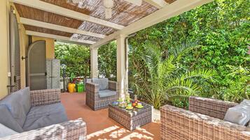 A covered outdoor seating area with wicker furniture and a table set with fruits and cups.