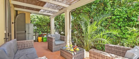 A covered outdoor seating area with wicker furniture and a table set with fruits and cups.
