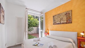 Een hotelkamer met een bed, een zithoekje, een nachtkastje, een raam met gordijnen en een schilderij aan de muur.