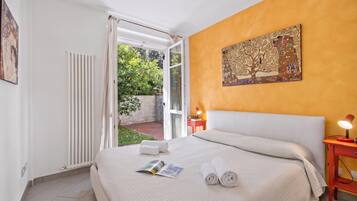 A hotel room with a bed, a reading area, a nightstand, a window with curtains, and a painting on the wall.
