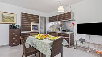 A modern kitchen with a dining area, a flat-screen TV, and a laptop on a cart.