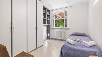 A bedroom with a bed, a window, a radiator, a bookshelf, and a wardrobe.