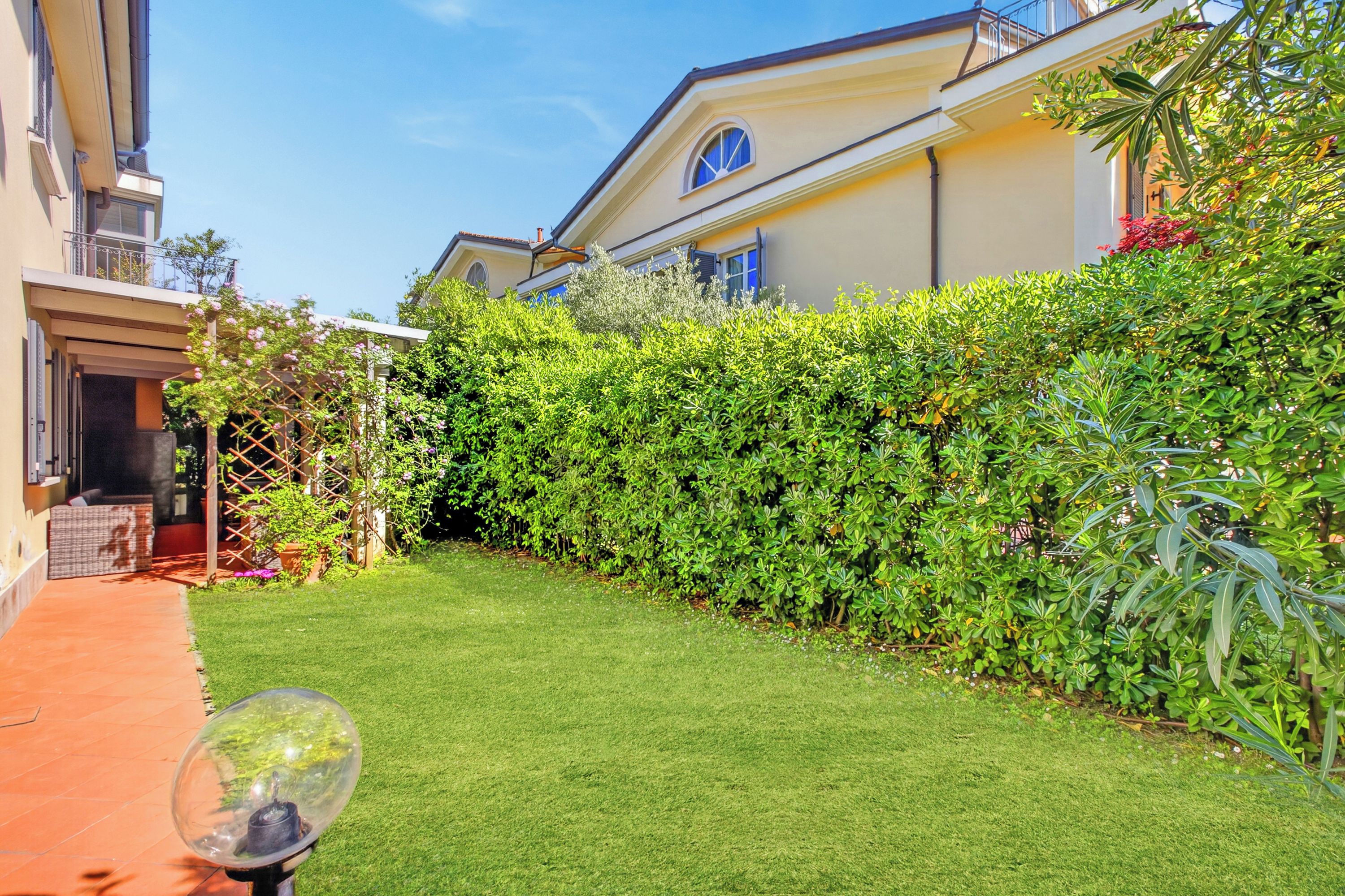 A well-maintained garden with a clear pathway, a hedge, and a building with a balcony.