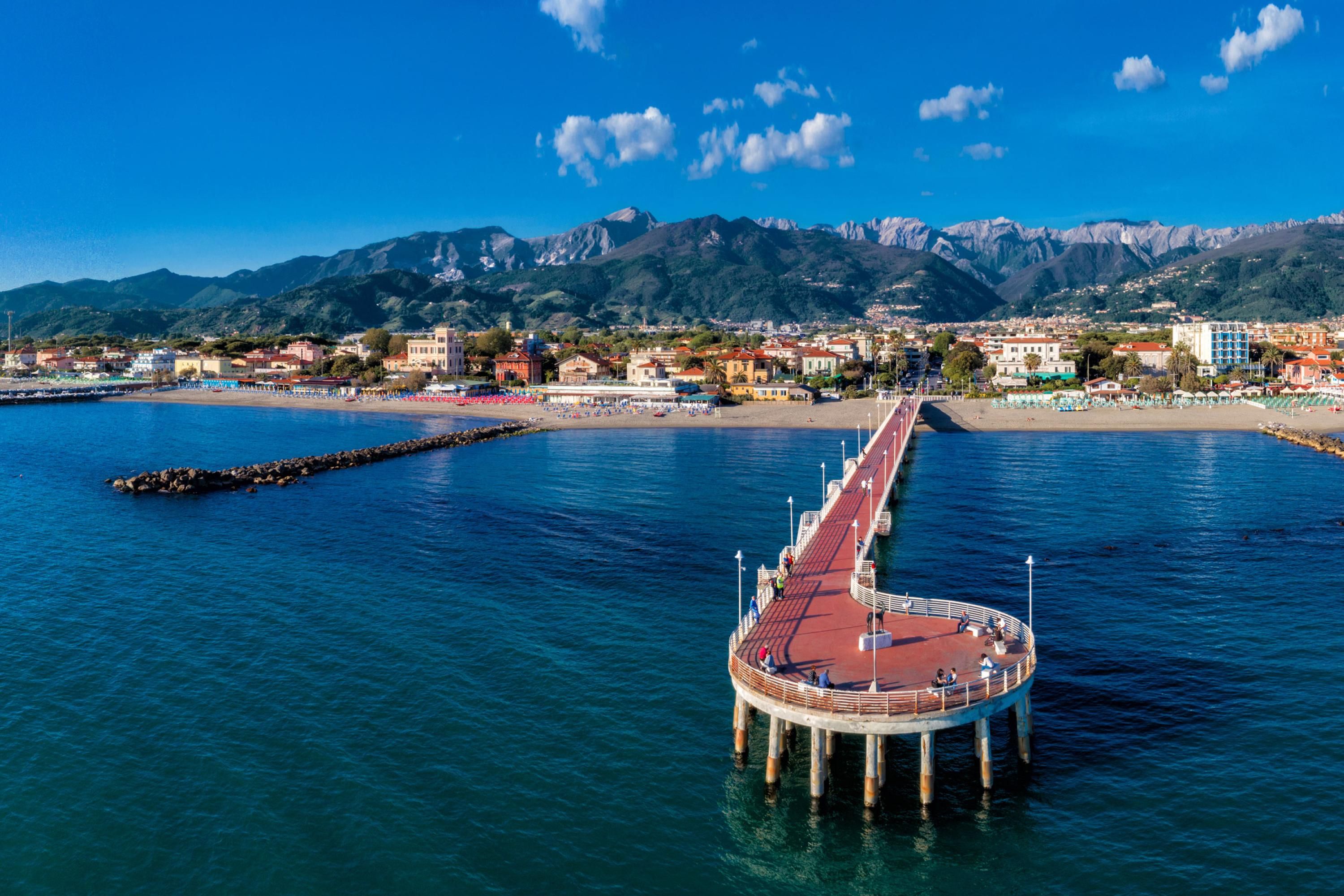 A pier extending into a calm sea with a mountainous backdrop.