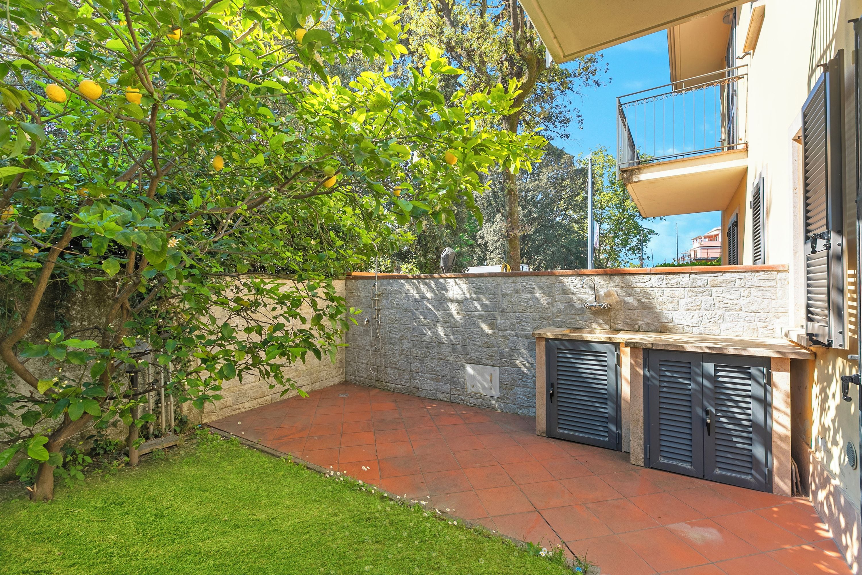A courtyard with a stone wall, a tree with lemons, and a tiled patio.