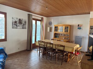 A dining area with a wooden table, chairs, a cabinet with glass doors, and a window with curtains. - Seaside (La Tranche-sur-Mer)