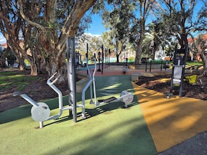 An outdoor exercise area with various fitness equipment, surrounded by trees and a clear sky. - Apartment in the Heart of Bondi (Sydney)