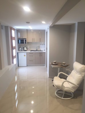 A compact kitchen with a microwave, kettle, and small refrigerator. There is a dining area with a chair and table, and a glass partition separates the kitchen from the living space. - Apartment in the Heart of Bondi (Sydney)