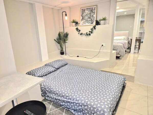 A small, modern bedroom with a bed, bedside table, and a potted plant. - Apartment in the Heart of Bondi (Sydney)