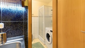 A compact bathroom with a sink, a washing machine, and a shower enclosure.