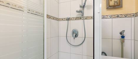 A shower with a handheld showerhead and a wall-mounted faucet.