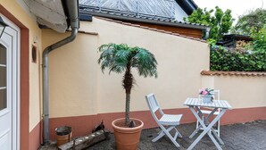 A small patio area with a potted palm tree, a white folding chair, and a table with a flower vase.