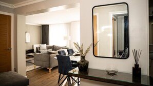 Un salon moderne avec un canapé, des fauteuils, une table basse en verre, un miroir et un vase avec des plantes.