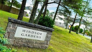 Uma placa de pedra com a inscrição 'Windsor Gardens', rodeada por relva e árvores.