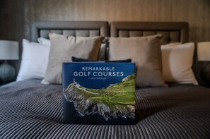 Un livre intitulé « Les plus beaux parcours de golf » de Iain Spragg, posé sur un lit avec une tête de lit et des oreillers.