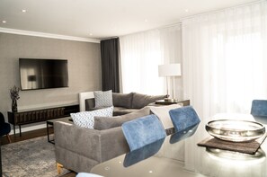 Un salon moderne comprenant un canapé, un téléviseur à écran plat, une lampe et un coin repas avec une table et des chaises.