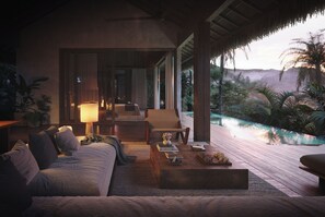 Una habitación acogedora con un sofá, una mesa de centro y una lámpara. Se ve una piscina y follaje por la ventana.