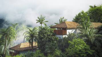 A thatched-roof building surrounded by lush greenery and clouds.