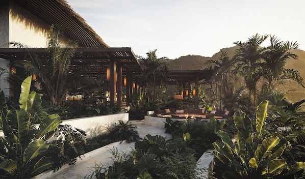 A resort with a covered outdoor seating area, lush tropical vegetation, and a thatched-roof structure. - Casa Tuya Ubud (Taro)