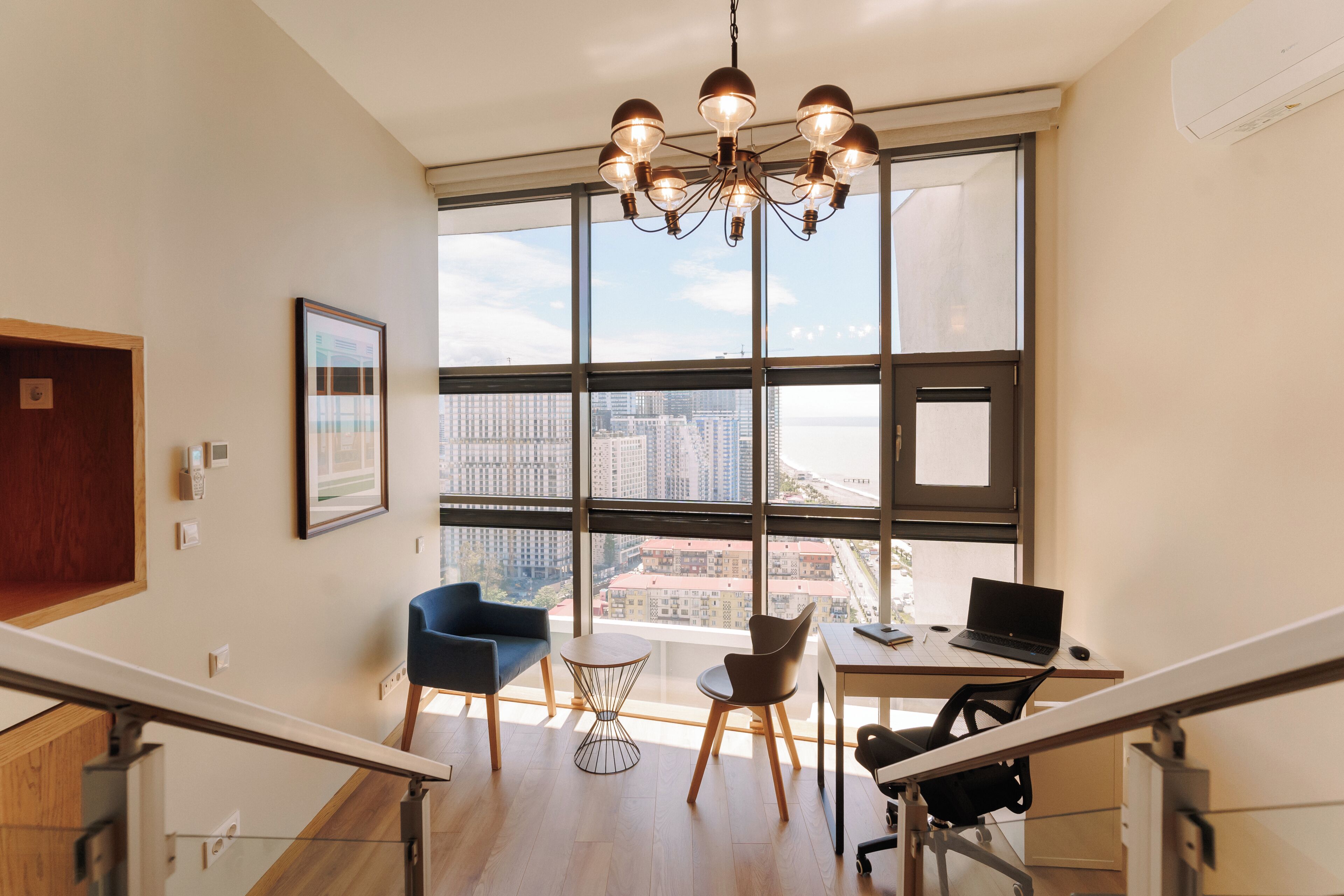 A modern office space with a large window, a desk with a laptop, and a chair.