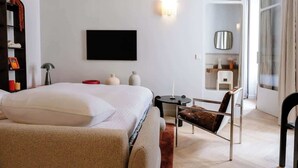 Ein modernes Hotelzimmer mit Bett, Schreibtisch, Stuhl, Fernseher und einem durchgehenden Tür zugehörigen Badezimmer.