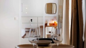 Ein Essbereich mit Tisch für vier Personen, einem Spiegel über dem Tisch und Blick auf einen Raum mit Bett und Nachttisch.