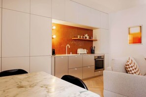 Eine kompakte Küche mit modernen Geräten, ein Essbereich mit einem Marmortisch und ein gemütlicher Wohnbereich mit einer Couch.