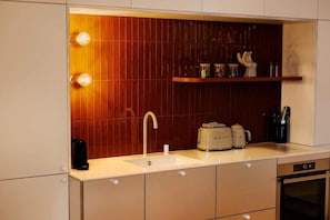 Eine moderne Küche mit einer weißen Spüle, zwei Wasserkochern, einer Kaffeemaschine und einem Toaster.