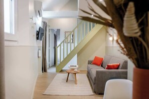 A modern living room with a staircase, a grey sofa with red cushions, a white coffee table, and a potted plant. - Babylon Popincourt 22 (Paris)