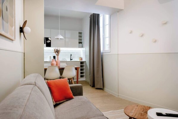 A modern living room with a sofa, a small round table, and a dining area in the background. - Babylon Popincourt 22 (Paris)