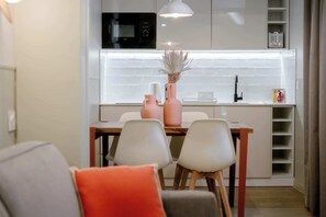 A modern kitchen with a microwave, a white countertop, and a dining area with chairs and a table. - Babylon Popincourt 22 (Paris)