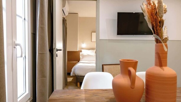 A hotel room with a bed, a TV mounted on the wall, and a table with two vases. - Babylon Popincourt 13 (Paris)
