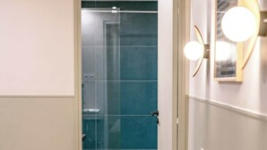 A room with a yellow sofa, a white pillow, a glass door leading to a bathroom, and a wall-mounted light fixture. - Babylon Popincourt 13 (Paris)